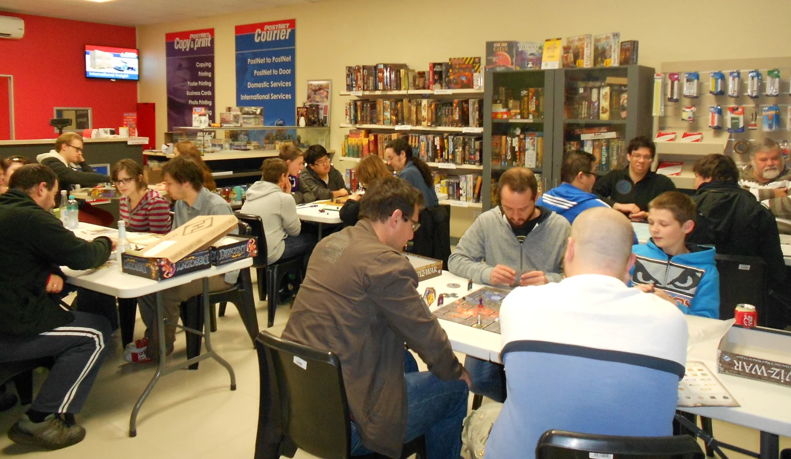 Players gathered around a table playing board games. A countertop and banners for business services is visible in the background